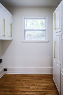 Yeni yenilenmiş, ahşap döşemeleri olan boş bir çamaşır odasında zarif altın ve ince donanımlı beyaz titreşimli dolaplar..