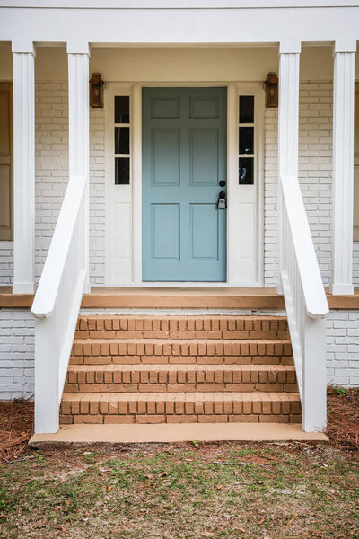 The front exterior entrance of a newly aqua blue painted front door on a white brick ranch style house with brick steps.