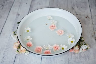 Süt banyosunda bir sürü taç yaprağı ve beyaz ahşap zeminde bir çiçek..