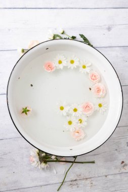 Süt banyosunda bir sürü taç yaprağı ve beyaz ahşap zeminde bir çiçek..