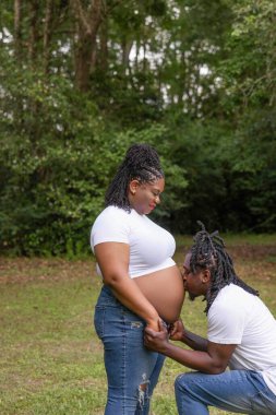 Güzel bir Afro-Amerikan çift anne portresi için poz veriyor. Diz çöküp annelerinin karnını öpüyor..