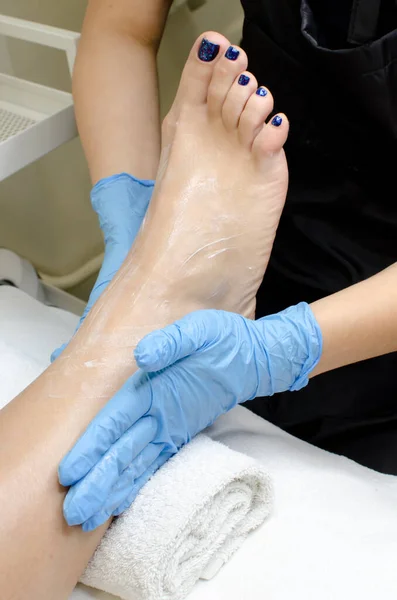 Foot massage with moisturizing or peeling cream by pedicurist hands wearing blue gloves, close up.