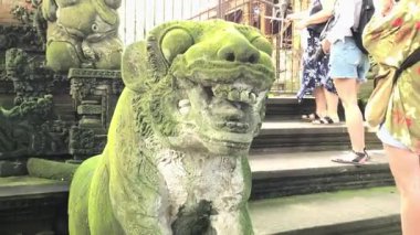Yosun kaplı geleneksel taş heykeller, koruyucu aslanlar veya efsanevi figürlerin yer aldığı canlı bir çekim. Arka planda, kadın gibi görünen çok sayıda turist çevreyi gözlemliyor.