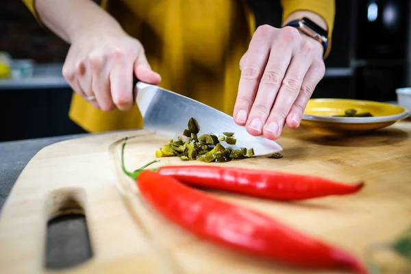 Woman cutting green spicy pepper jalapeno on wooden cutting board in the kitchen. Defocused. High quality photo