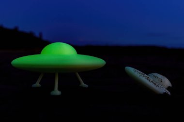 Gece çakılmış bir UFO 'nun yanında parlayan bir uçan sos duruyor. Cep telefonuyla çekilmiş sahte bir fotoğrafı taklit etmek için kasıtlı olarak düşük kalite fotoğraf..