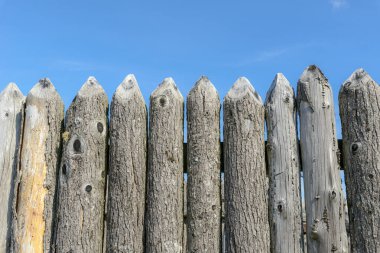 Kalenin solmuş, eski bir tahta duvarına yakın çekim. Üstleri keskinleştirilmiş. Yukarıdaki mavi gökyüzü. Peyzaj yönelimi.