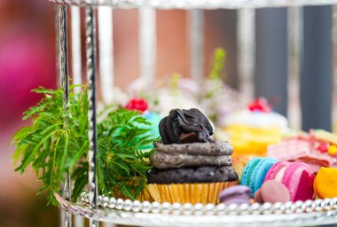 Öğleden sonra Çayı ya da Yüksek Çay Çiçek, makarna, çörek, kek, renkli arka planda gümüş rafta sergilenir