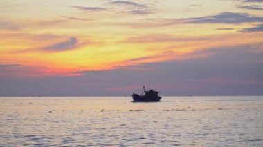 Şafakta açık sarı bulutlu bir arka planda Vietnamlı balıkçıların balıkçı teknelerinin siluetleriyle limana doğru koşan deniz manzarası. Deniz manzaralı gün doğumu ve günbatımı.