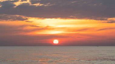 Denizin üzerindeki manzara. Güneş ufuktan yükseliyor. Bulutlu gökyüzü parlak turuncu sarıdır. Doğa denizi ve gökyüzü gün doğumunda ve batımında.