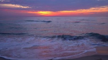 Sahil manzarasının şafak vakti yavaş hareket etmesi, turuncu-sarı güneş ışığında parıldayan denizin dalgalarıyla, renkli bulutlu bir gökyüzü ile güzel renklerle doludur. Gün batımı ve gün doğumu deniz manzarası. Alacakaranlık.