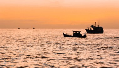 Şafak vakti deniz burnu, Binh Minh 'in sarı-turuncu ışıklı arka planına sahip Vietnamlı balıkçı balıkçı teknelerinin siluetleriyle. Deniz manzarası kavramı ve deniz çalışmaları.