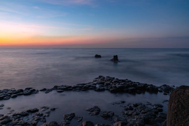 Fotoğraf, milyonlarca yıl önce şafak sökerken, antik lav akıntılarındaki deniz manzarasını gözler önüne seriyor. Deniz manzarası ve jeoloji kavramı. Yumuşak odak.
