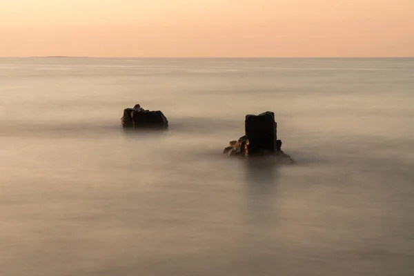 stock image Photo exposes a marine landscape in an ancient lava rock rapids millions of years ago, at dusk, with two lava rocks protruding above the sea. Warm photo color. Soft focus.