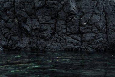 Milyonlarca yıl önce aşağıda su bulunan bir plajda soğuyan volkanik lav kayası. Siyah taş arka plan, keskin. Jeolojik kavram.