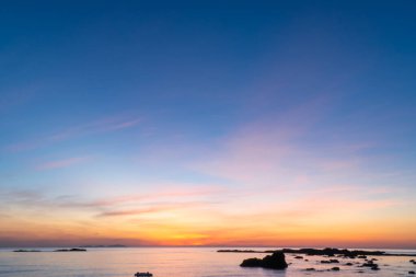Gün batımında gökyüzü ve deniz manzarası. Şafağın ince sarı ve mavi bulutlarıyla. Arkaplan açık mavi gökyüzü gün doğumu ve gün batımı.