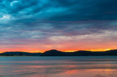 Sunrise at the beach with colourful high cloud filled sky and flat surf at Umina Point, Umina Beach on the Central Coast, NSW, Australia.