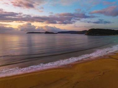 Gündoğumu yağmur bulutları ve hafif dalgalarla Orta Sahildeki Umina Sahili 'nde Ocean Beach, NSW, Avustralya.