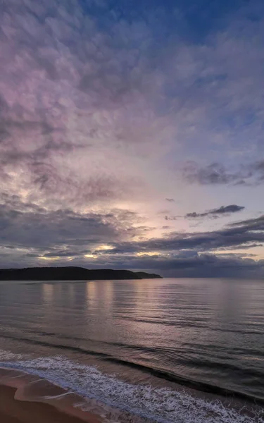 Sunrise with rain clouds and gentle waves at Ocean Beach in Umina Beach on the Central Coast, NSW, Australia.