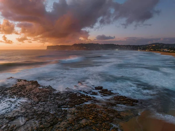 Dawn seascape with clouds,  rock platform, good size waves and plenty of atmosphere at North Avoca Beach on the Central Coast, NSW, Australia.