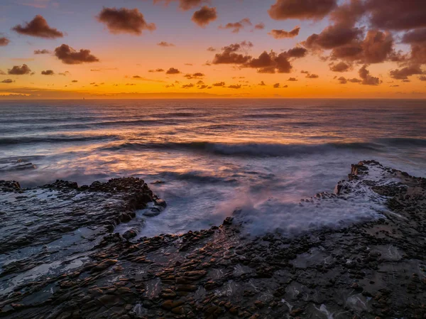 Dawn seascape with clouds, rock platform, good size waves and plenty of atmosphere at North Avoca Beach on the Central Coast, NSW, Australia.