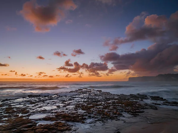 Dawn seascape with clouds,  rock platform, good size waves and plenty of atmosphere at North Avoca Beach on the Central Coast, NSW, Australia.