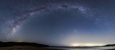 The Milky Way Panorama in the night sky with the lights from Palm Beach in Sydney on the horizon as viewed from Putty Beach on the Central Coast, NSW, Australia.