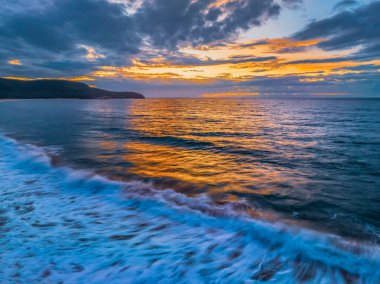 Central Coast, NSW, Avustralya 'daki Killcare Sahili' nde düz sörf ve bulutlarla gün doğumu denizi..