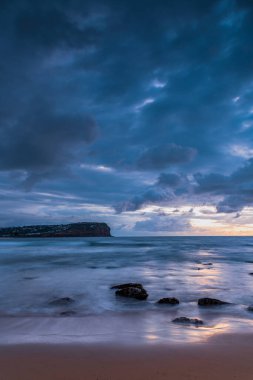 Central Coast, NSW, Avustralya 'daki Macmaster Sahili' nde yağmur bulutları ve kayalarla gün doğumu denizi..