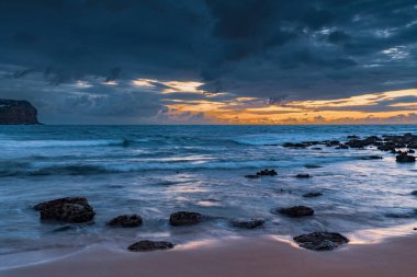 Central Coast, NSW, Avustralya 'daki Macmaster Sahili' nde yağmur bulutları ve kayalarla gün doğumu denizi..