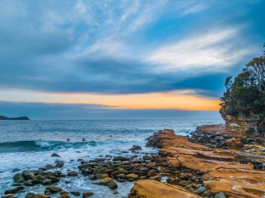 Gündoğumu deniz manzarası bulutlar, sörfçüler, dalgalar ve kayalar ile Avoca Sahili, NSW, Avustralya.