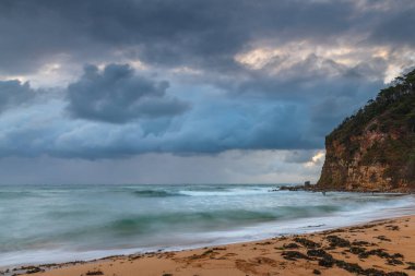 Yağmurlu gün doğumu bulutlu gökyüzü ve Orta Sahildeki Macmaster Sahili 'nde dalgalı dalgalar, NSW, Avustralya.