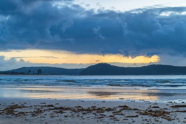 Gündoğumu deniz manzarası, yağmur bulutları ve kumsaldaki yansımalarla Orta Sahilde, NSW, Avustralya.