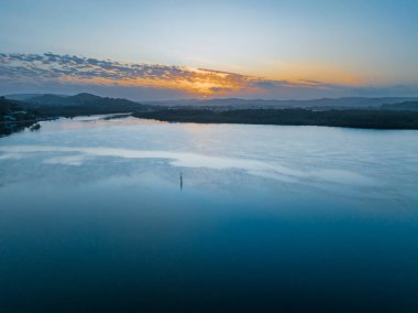 Körfezin üzerinde gün doğumu, ışık ve alçak bulut örtüsüyle Orta Sahildeki Woy Woy, NSW, Avustralya.