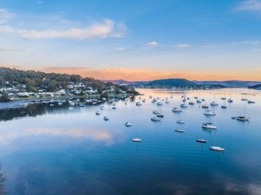 Körfezin üzerindeki gündoğumu, dağların eteklerine kurulmuş tekneler, mavi gökyüzü ve Orta Sahildeki Hardys Körfezi 'nde birkaç dağınık bulut, NSW, Avustralya.