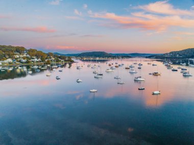 Körfezin üzerindeki gündoğumu, dağların eteklerine kurulmuş tekneler, mavi gökyüzü ve Orta Sahildeki Hardys Körfezi 'nde birkaç dağınık bulut, NSW, Avustralya.