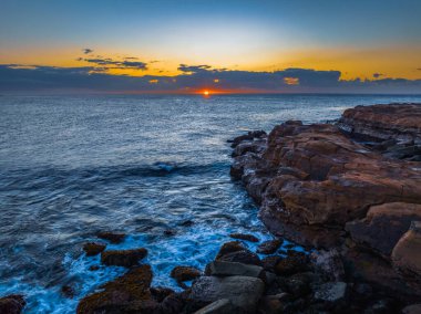 Gün doğumu deniz manzarası. Ufukta kayalar ve bulutlar var. Avoca Sahili 'nde, NSW, Avustralya..