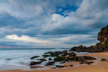Deniz kenarında, bulutlar, kayalar ve dalgalarla kasvetli bir gün doğumu Central Coast, NSW, Avustralya 'daki Killcare Sahili' nde..