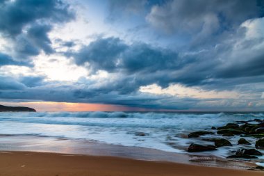 Deniz kenarında, bulutlar, kayalar ve dalgalarla kasvetli bir gün doğumu Central Coast, NSW, Avustralya 'daki Killcare Sahili' nde..