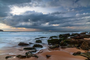 Deniz kenarında, bulutlar, kayalar ve dalgalarla kasvetli bir gün doğumu Central Coast, NSW, Avustralya 'daki Killcare Sahili' nde..