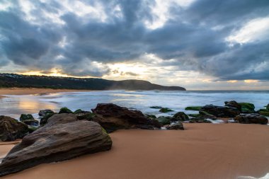 Deniz kenarında, bulutlar, kayalar ve dalgalarla kasvetli bir gün doğumu Central Coast, NSW, Avustralya 'daki Killcare Sahili' nde..