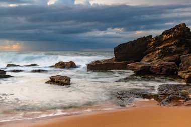 Deniz kenarında, bulutlar, kayalar ve dalgalarla kasvetli bir gün doğumu Central Coast, NSW, Avustralya 'daki Killcare Sahili' nde..