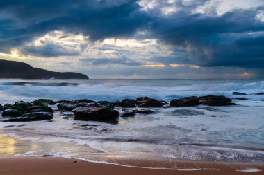 Deniz kenarında, bulutlar, kayalar ve dalgalarla kasvetli bir gün doğumu Central Coast, NSW, Avustralya 'daki Killcare Sahili' nde..