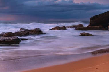 Deniz kenarında, bulutlar, kayalar ve dalgalarla kasvetli bir gün doğumu Central Coast, NSW, Avustralya 'daki Killcare Sahili' nde..