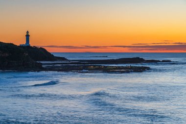 Düşük bulut kütleli gündoğumu denizi ve Orta Sahildeki Asker Sahili 'nden Norah Head Deniz feneri, NSW, Avustralya.