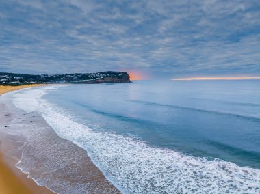 Gökyüzü bulutlarla doluyken hava gündoğumu ve Orta Sahildeki Macmaster Sahili 'nde küçük dalgalar, NSW, Avustralya.
