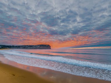 Gökyüzü bulutlarla doluyken hava gündoğumu ve Orta Sahildeki Macmaster Sahili 'nde küçük dalgalar, NSW, Avustralya.