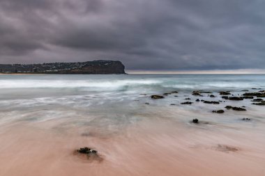 Central Coast, NSW, Avustralya 'daki Macmaster Sahili' nde küçük dalgalarla bulutlu gün doğumu deniz manzarası.