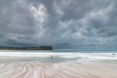 Central Coast, NSW, Avustralya 'daki Macmaster Sahili' nde küçük dalgalarla bulutlu gün doğumu deniz manzarası.
