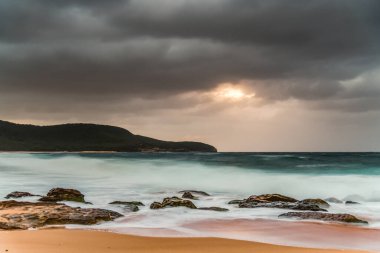 Central Coast, NSW, Avustralya 'daki Killcare Sahili' nde yağmur bulutlarıyla birlikte rüzgarlı ve çalkantılı bir gün doğumu..