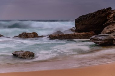 Central Coast, NSW, Avustralya 'daki Killcare Sahili' nde yağmur bulutlarıyla birlikte rüzgarlı ve çalkantılı bir gün doğumu..